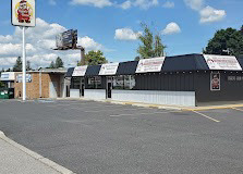 Restaurant building with black awnings, brick entrance, and signage across the front, located next to a large parking lot under a partly cloudy sky.